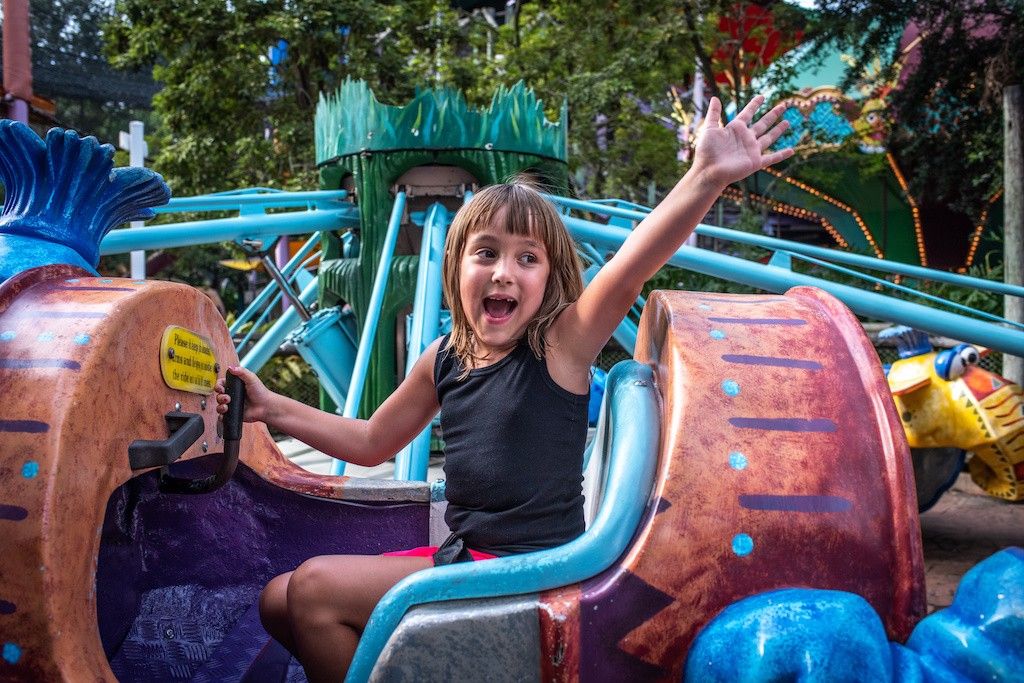 Child waving from a colorful amusement park ride
