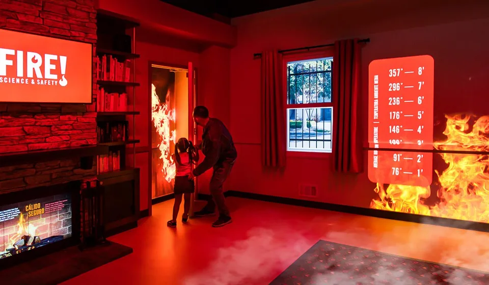 Visitors in the simulated home at Fire! Science & Safety, with projected flames and safety information