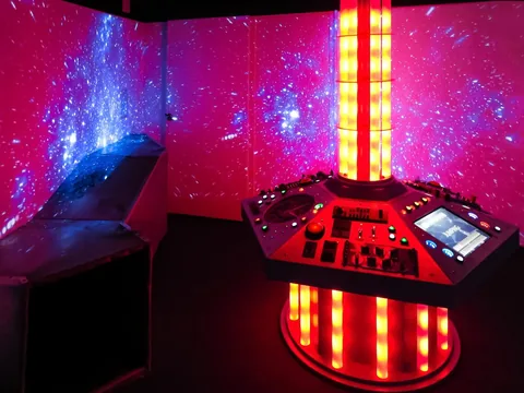 The illuminated SATTA control console surrounded by projected space imagery at Pennypickle’s Workshop